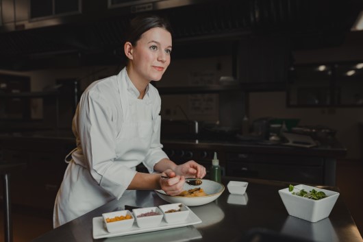 Oliva Sewell in a commercial kitchen plating some food